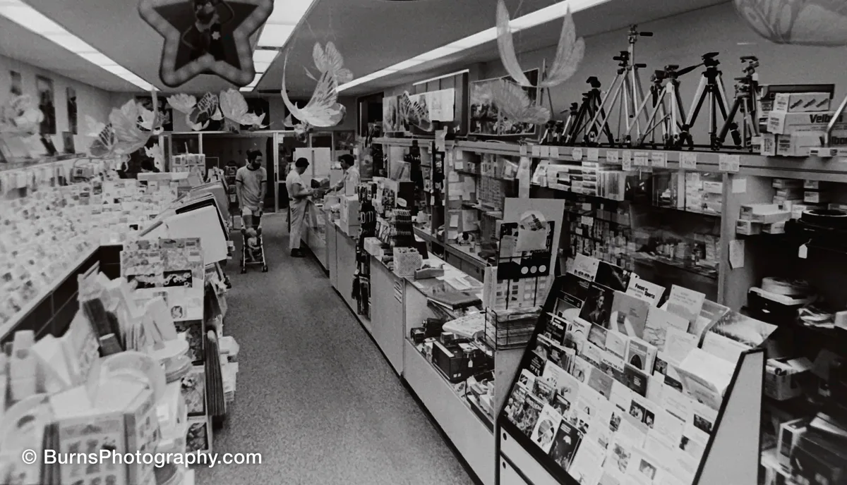 Camera store interior with glass counters, tripods on a high shelf, and paper decorations hanging from the ceiling