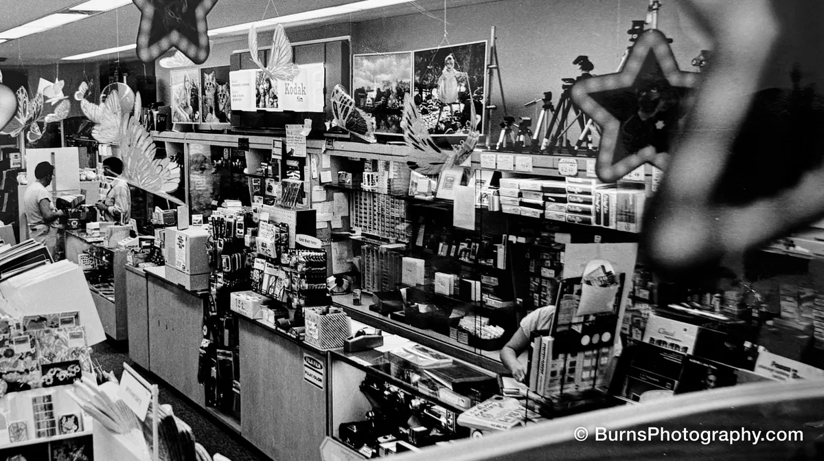 Black and white interior of the Hilldale Card & Camera store in Madison, Wisconsin with glass counters, film displays, tripods and hanging star ornaments