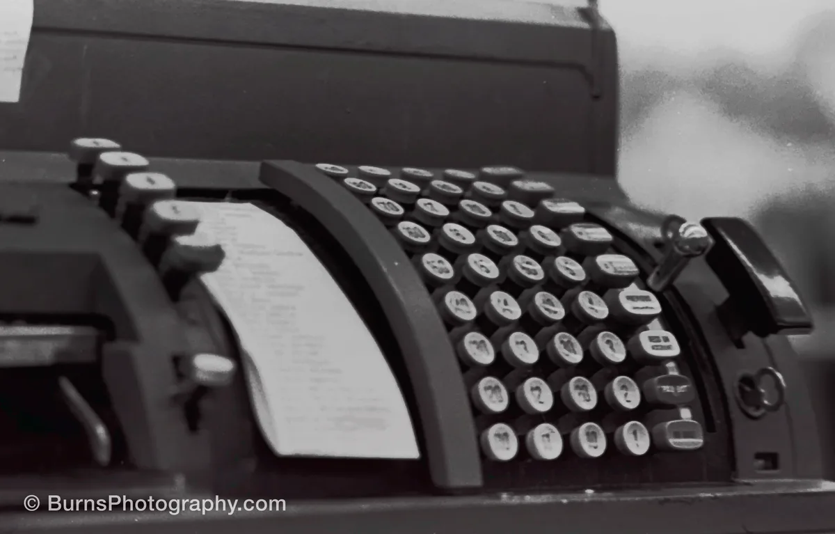 Black and white close-up of a mechanical cash register with rows of round keys and a paper notes