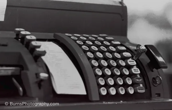 Black and white close-up of a mechanical cash register with rows of round keys and a paper notes