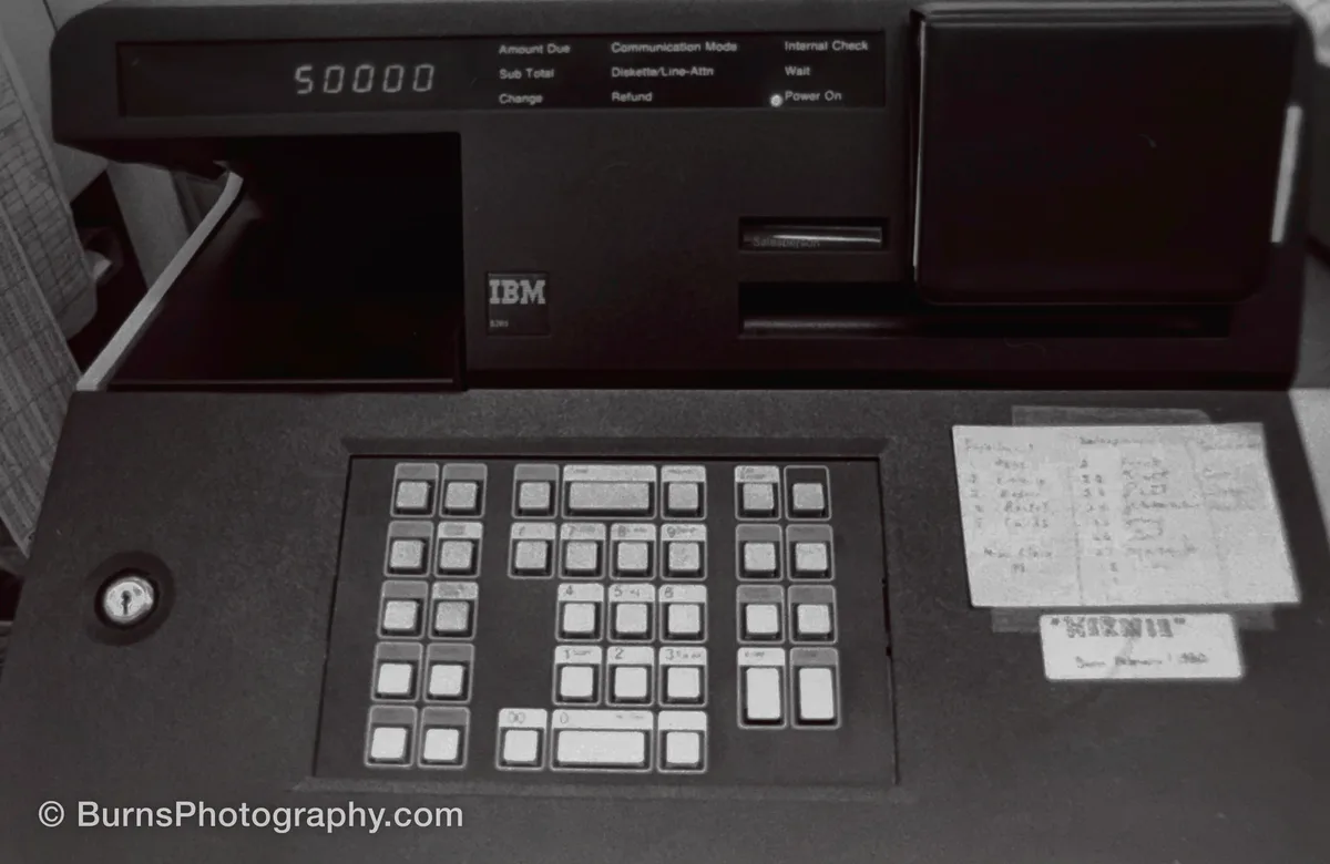 Black IBM cash register terminal with numeric keypad, lit display reading 50000, and taped handwritten note