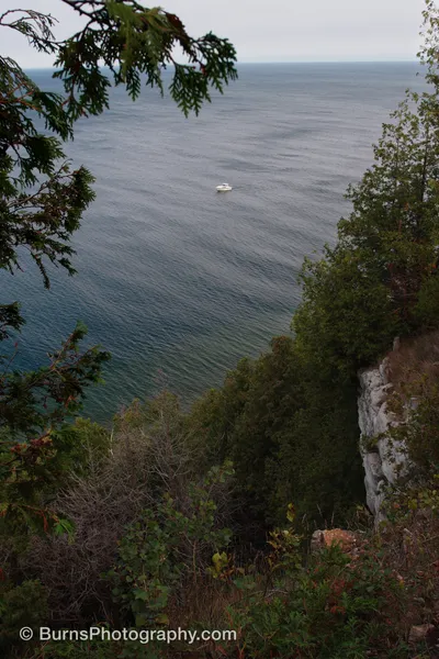 View from a wooded limestone bluff over calm water with a small white boat anchored offshore