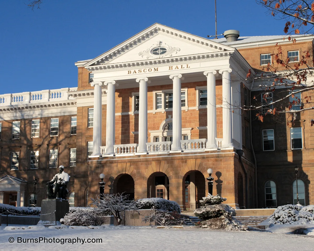 Bascom Hall's white columned portico and sandstone facade above a snow-covered hill with the seated Lincoln statue