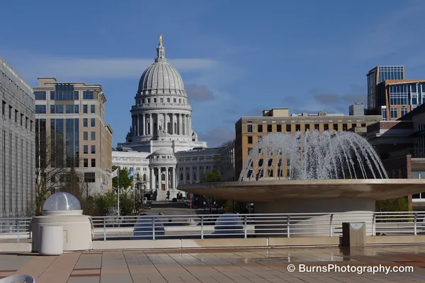 Wisconsin State Capitol dome beyond downtown buildings, with an arcing disc fountain on a rooftop terrace