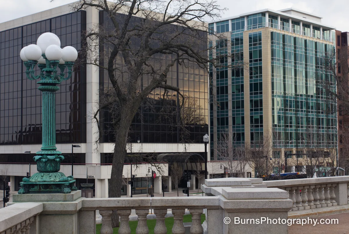 Verdigris lamppost and stone balustrade in front of mirrored office buildings with a bare tree