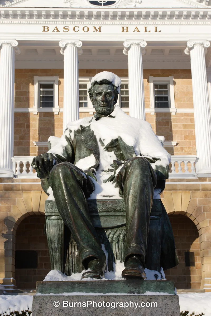 Bronze seated Lincoln statue covered in snow in front of white columns and Bascom Hall lettering