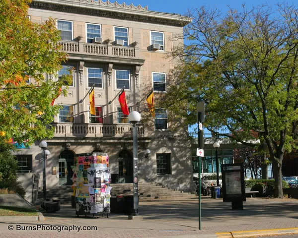 Limestone university union building with red and yellow banners, poster-covered kiosk, and autumn trees