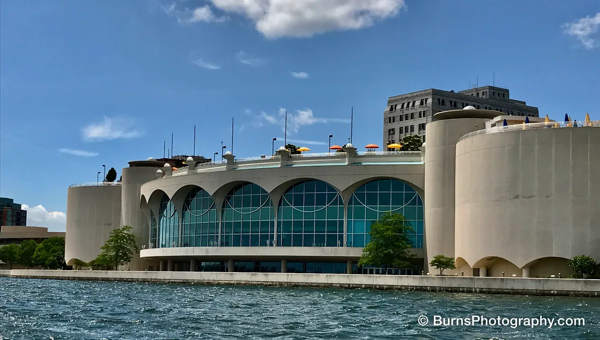 Curved concrete and glass lakefront building with arched windows and rooftop umbrellas above choppy water
